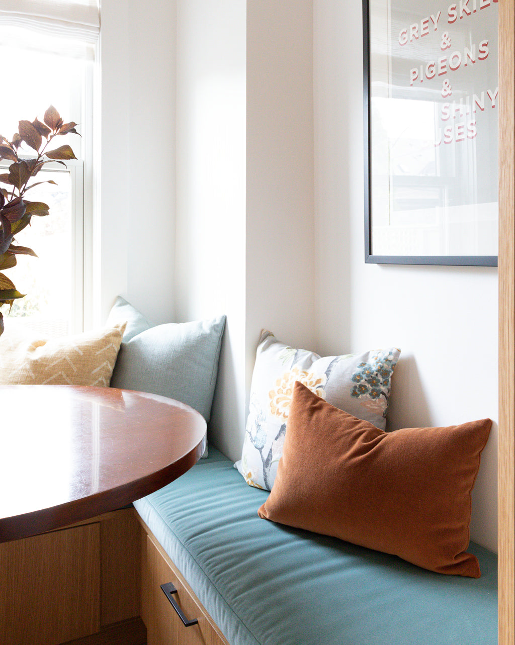 Breakfast nook with round wood table and rattan light fixture. Custom bench pillows by Hemme