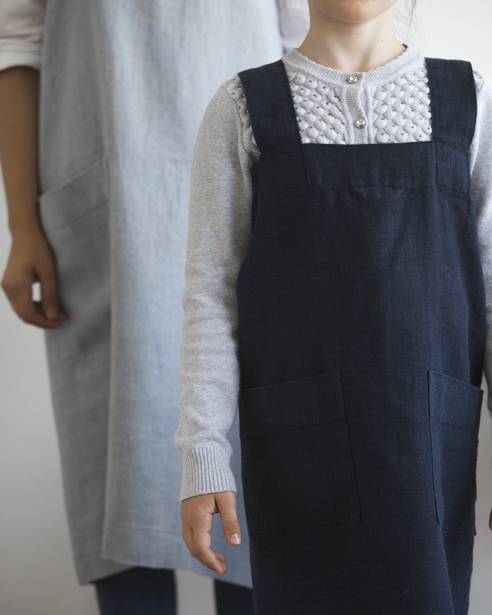 Child wearing Mini kids linen smock apron with adult behind wearing adult smock apron by Hemme