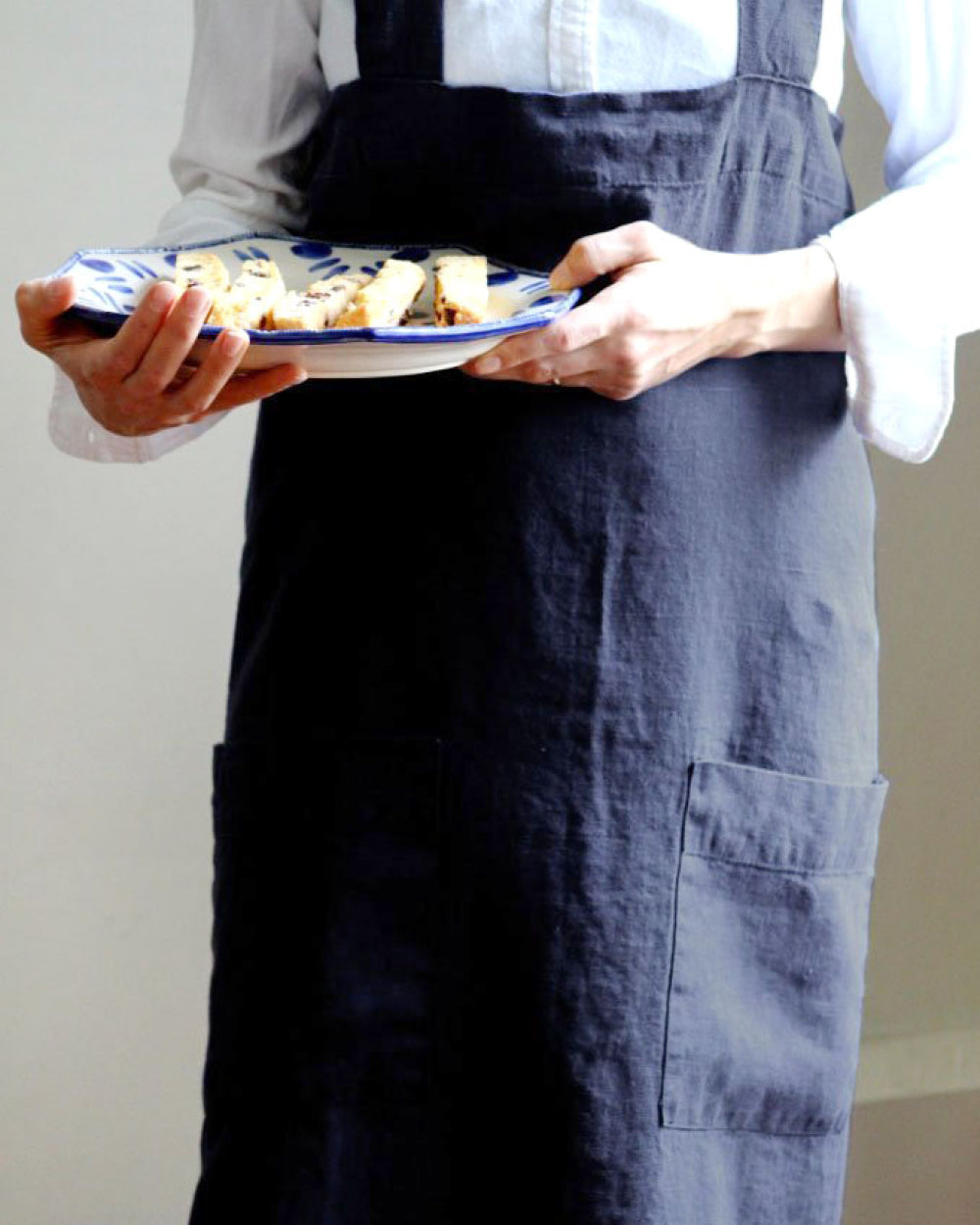 Person holding plate with food and wearing Annie Linen Smock Apron in Ink Blue