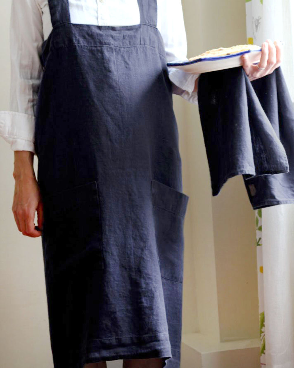 Person holding plate with food and wearing Annie Linen Smock Apron in Ink Blue
