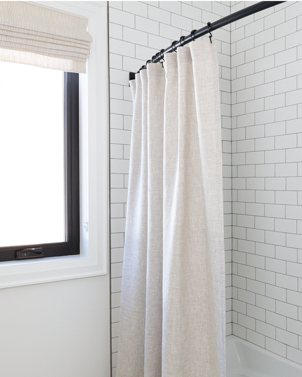Natural linen shower curtain hanging in white tiled shower