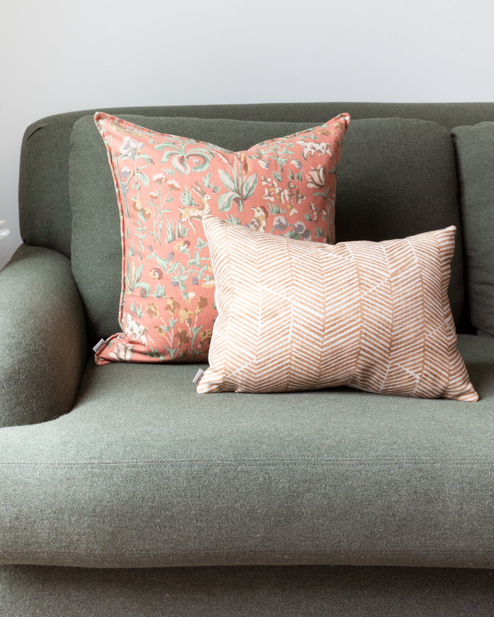 Rectangle rust chevron Imogen Heath patterned pillow sitting on green sofa with floral square complimentary pillow behind it.