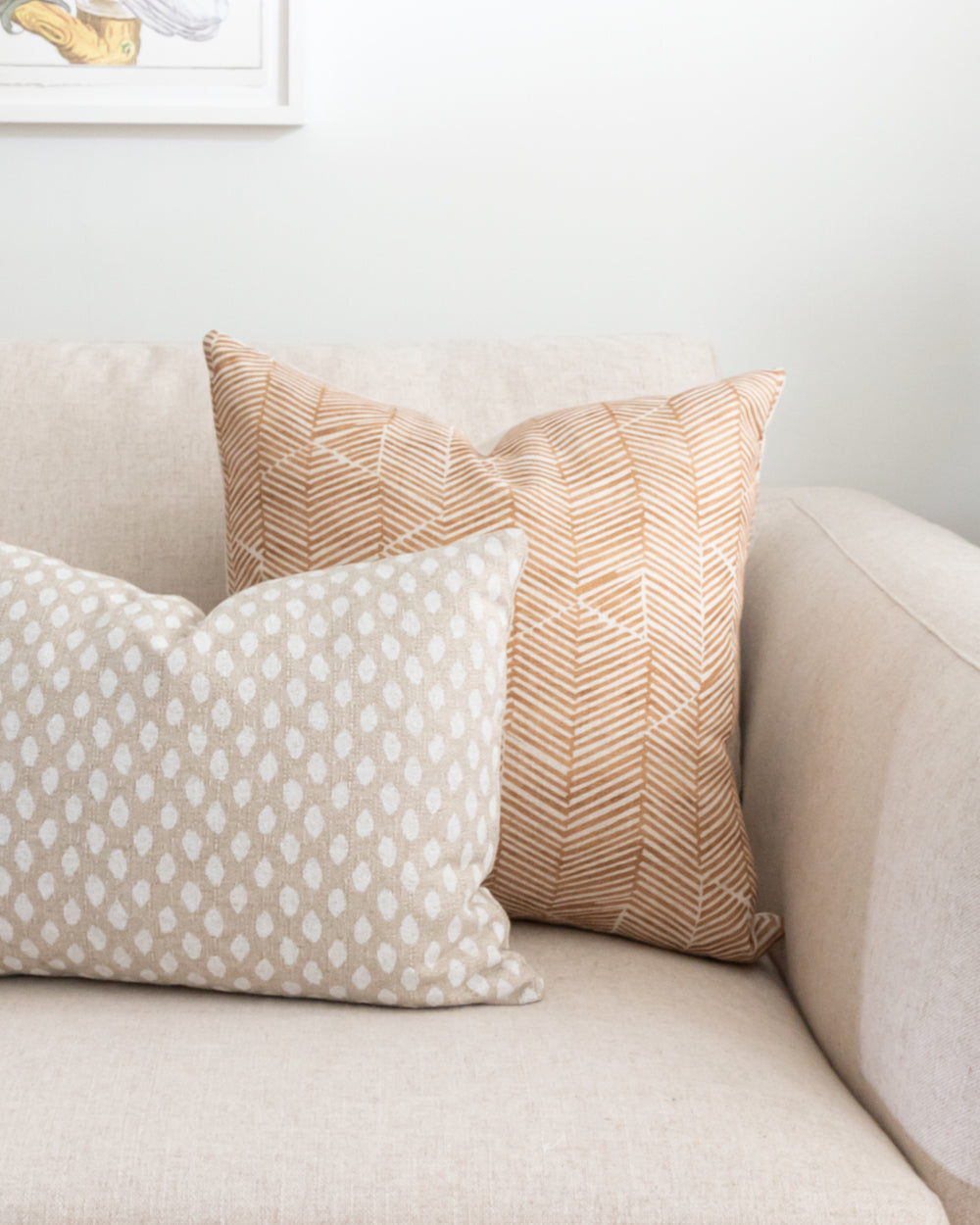 Rust chevron Imogen Heath patterned pillow on white sofa with rectangle polka dot pillow.