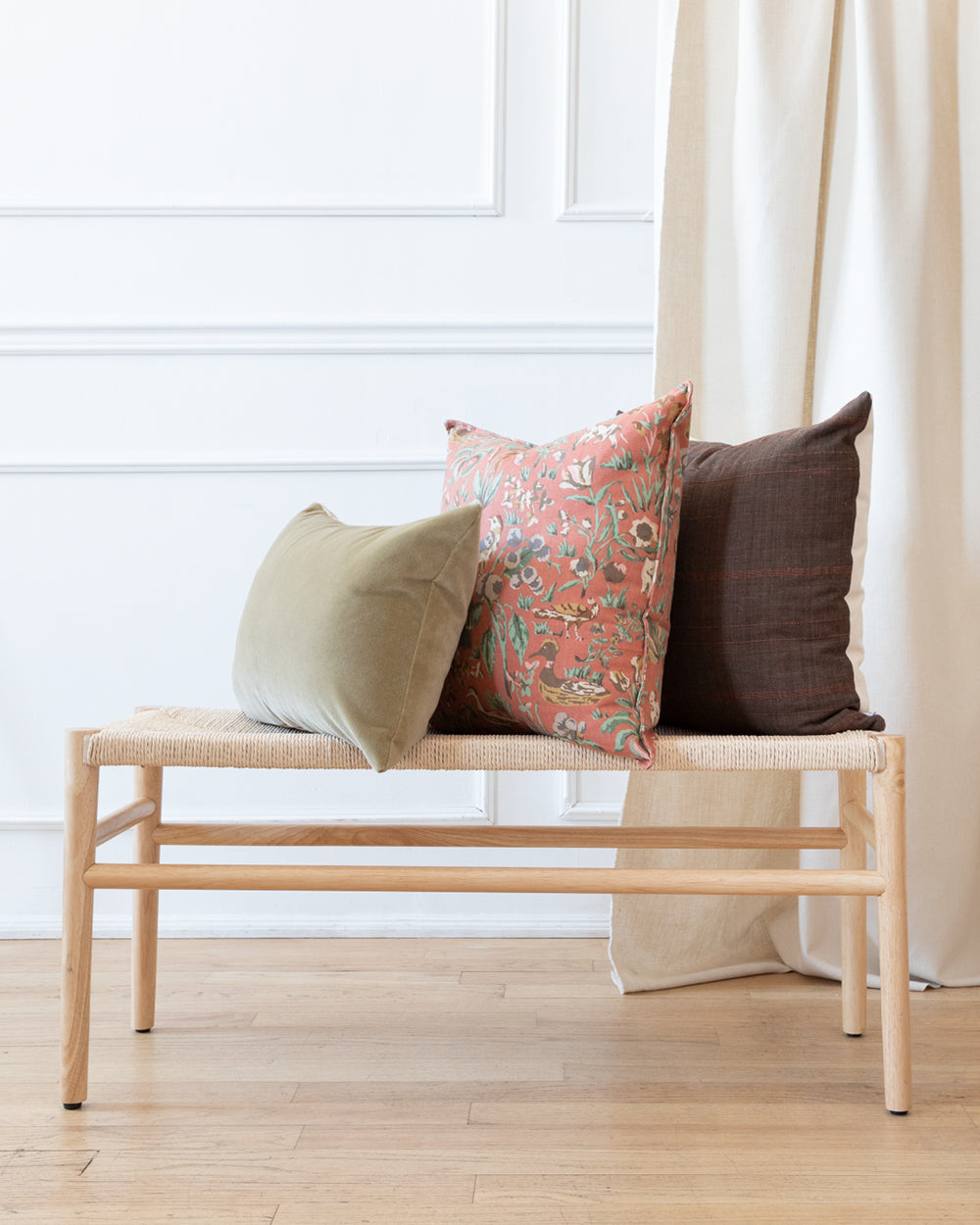 Square brown toned striped cotton pillow with floral and mohair green complimentary pillows, sitting on natural wood bench.