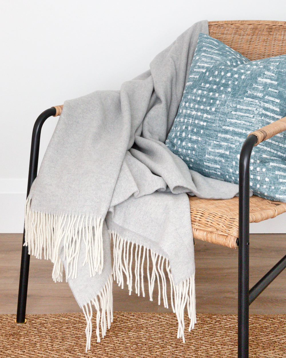 Close up detail of Haliburton grey wool throw with fringe sitting on rattan chair with blue pillow
