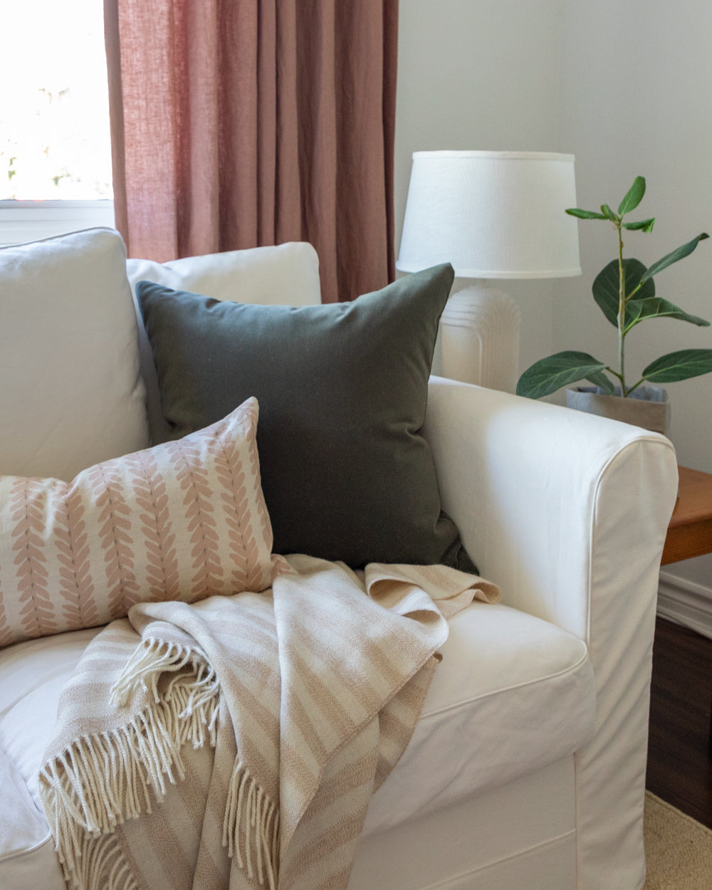 Dark forest green velvet pillow sitting on a white sofa along with a blush chevron lumbar pillow and striped throw