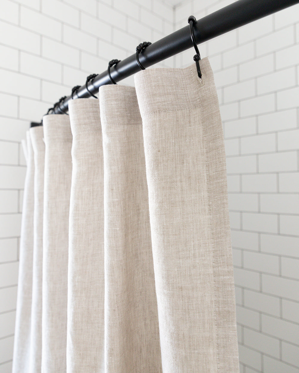 Detail close up of natural linen shower curtain hanging in white tiled shower
