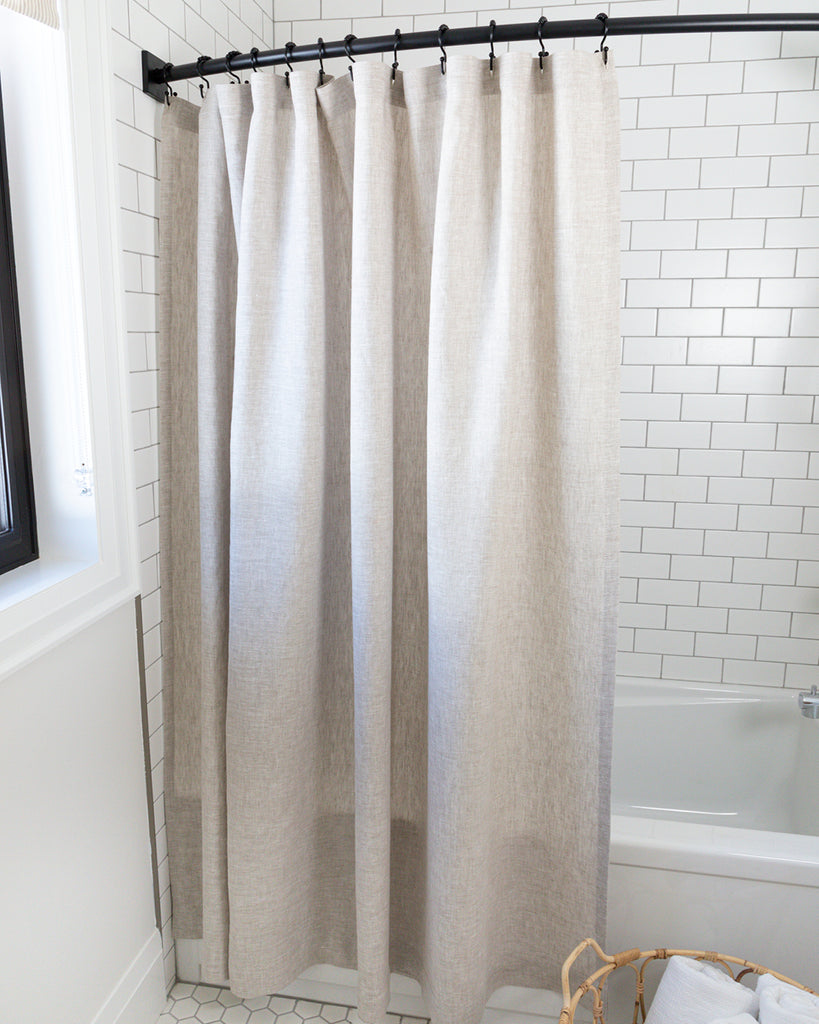 Natural linen shower curtain hanging in white tiled shower