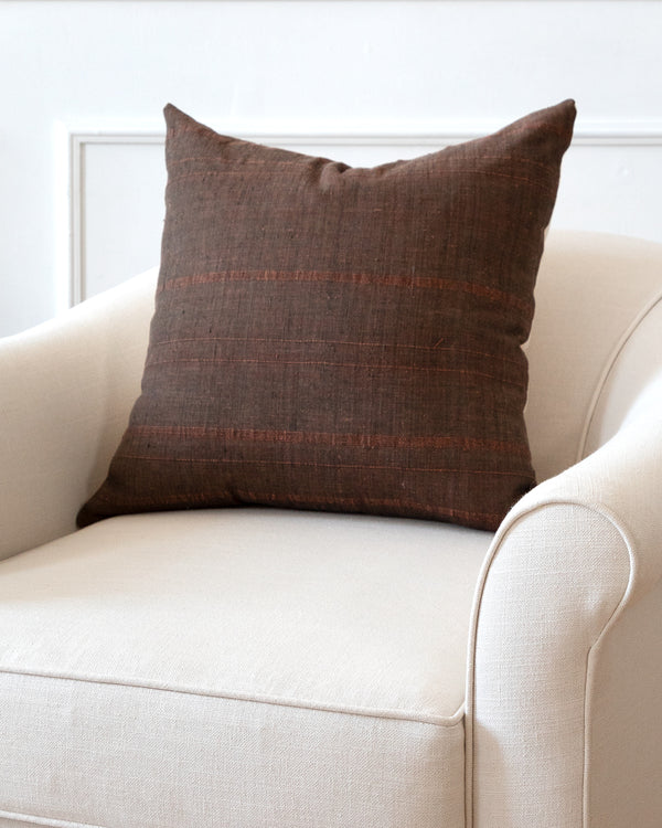 Square brown toned striped cotton pillow sitting on white arm chair.