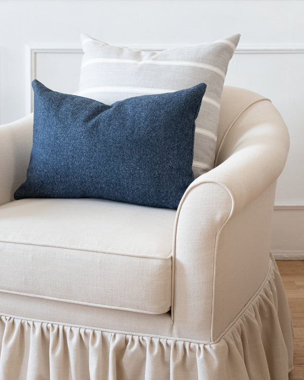 Rectangle inky blue wool pillow sitting on white sofa chair with complimentary grey striped square pillow.