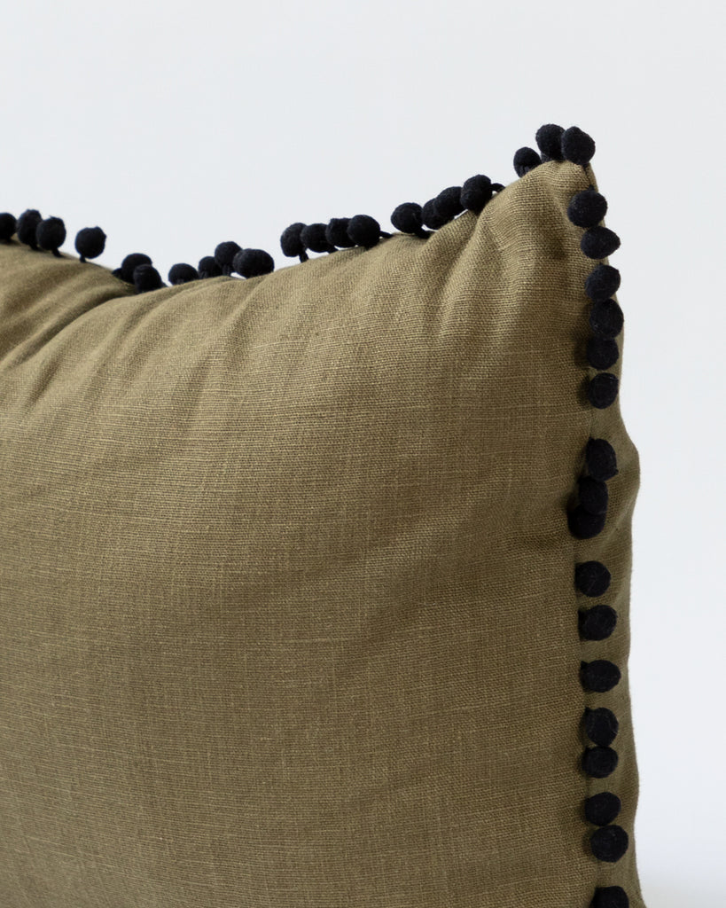 Detail close up of pom pom olive green linen lumbar pillow.