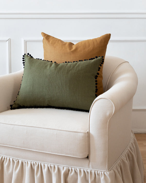 Pom pom olive green linen lumbar pillow on white sofa with square rust complimentary pillow.