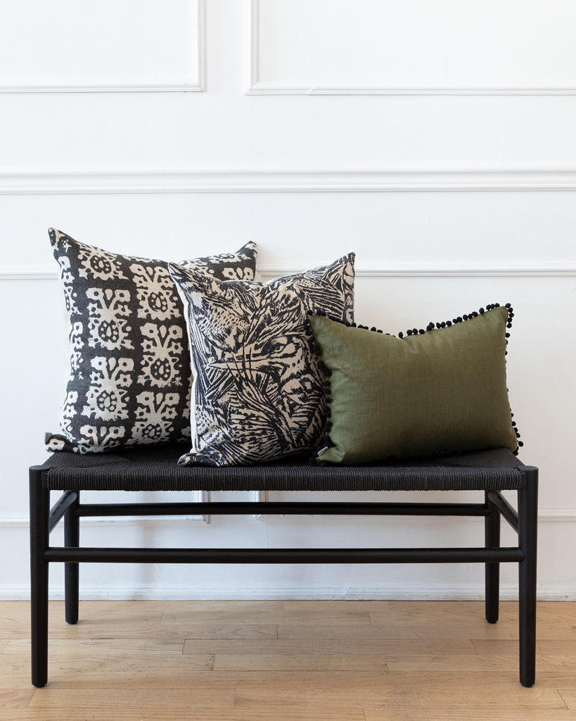 Pom pom olive green linen lumbar pillow with complimentary black and white pillows on black bench.
