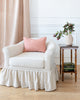 Rectangle embroidered pink pillow sitting on white armchair.