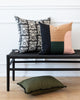 Dunne Quilted Cotton Pillow in black, green, pink and brown sitting on a black bench with complimentary pillow.