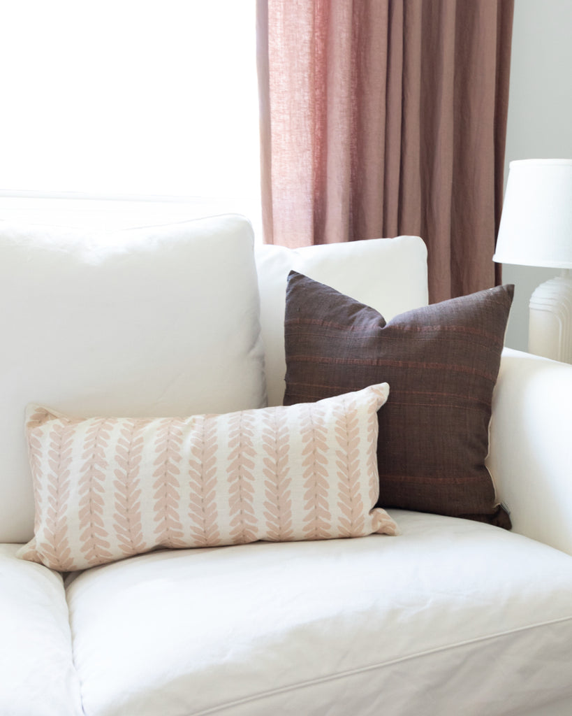 Blush linen botanical stripe lumbar pillow sitting on white sofa with brown linen complimentary pillow