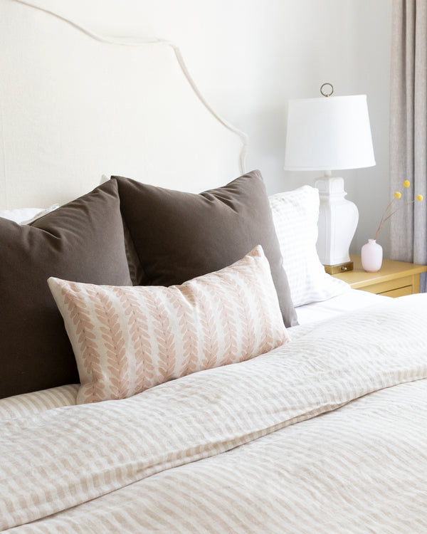 Blush linen botanical stripe lumbar pillow sitting on striped duvet bed with complimentary mohair brown pillows