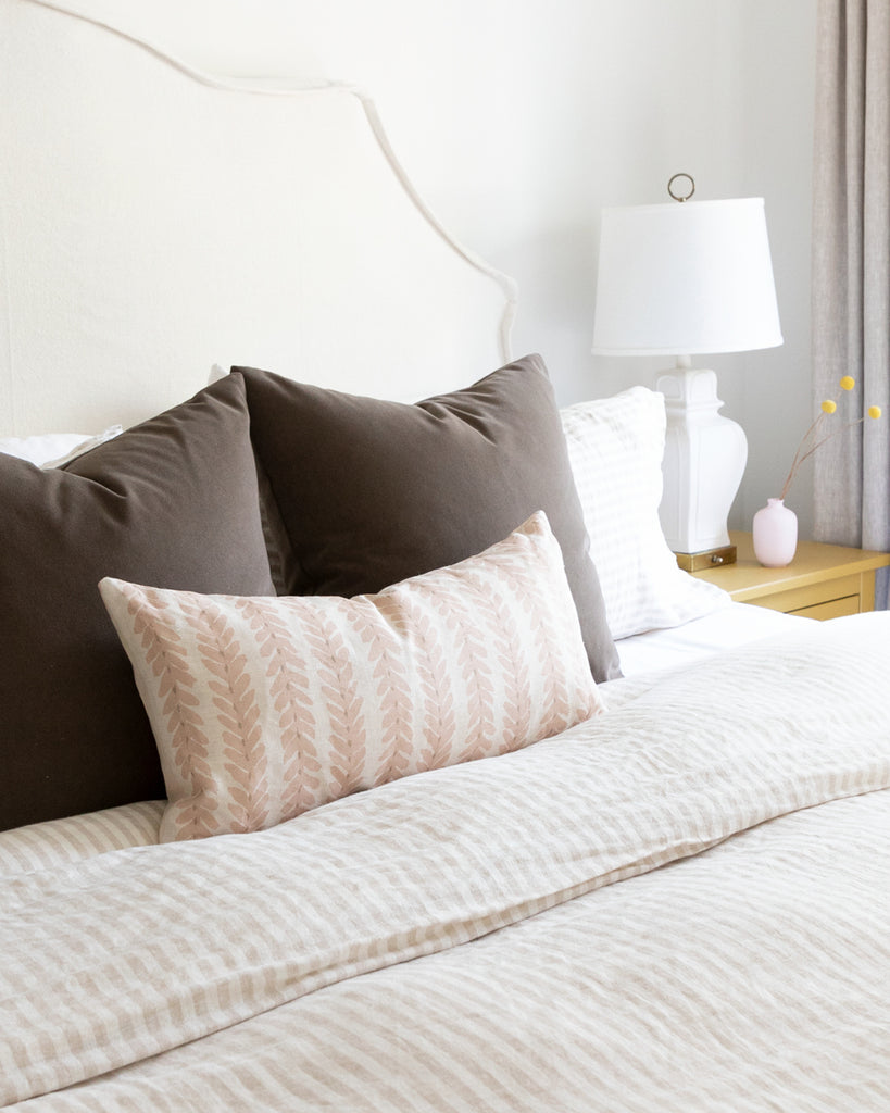 Blush linen botanical stripe lumbar pillow sitting on striped duvet bed with complimentary mohair brown pillows