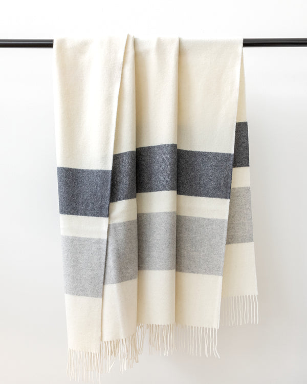 Lush stone greys and cream throw blanket hanging on black rod.