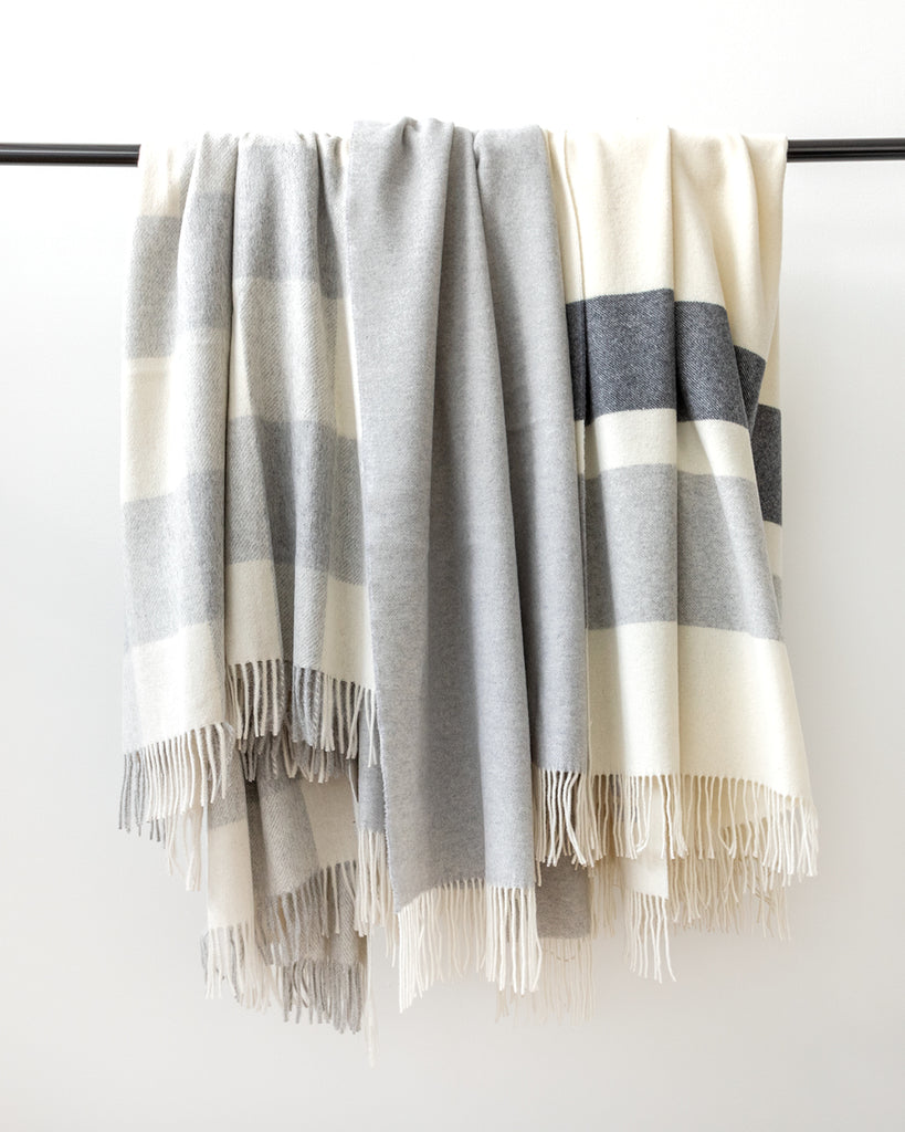 Collection of three varying grey and cream lush throw blankets hanging on black rod.