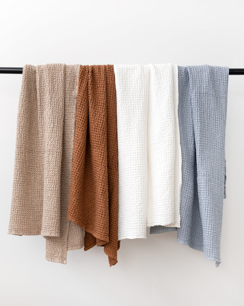 Row of different coloured waffle bath towels hanging on back rod.
