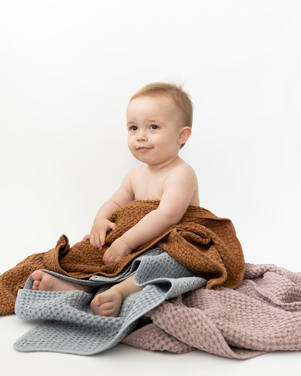 Baby wrapped in three Hooded Waffle Towels in colours cinnamon, blue grey and woodrose. 
