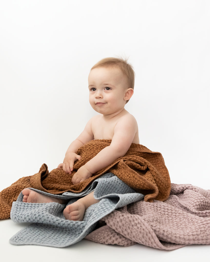 Sitting baby wrapped up in three waffle bath towels.
