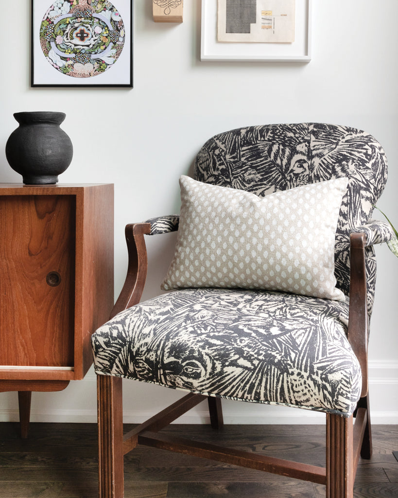 Rectangle ikat inspired dot pillow in a creamy white on a natural beige background sitting on a black and white abstract arm chair