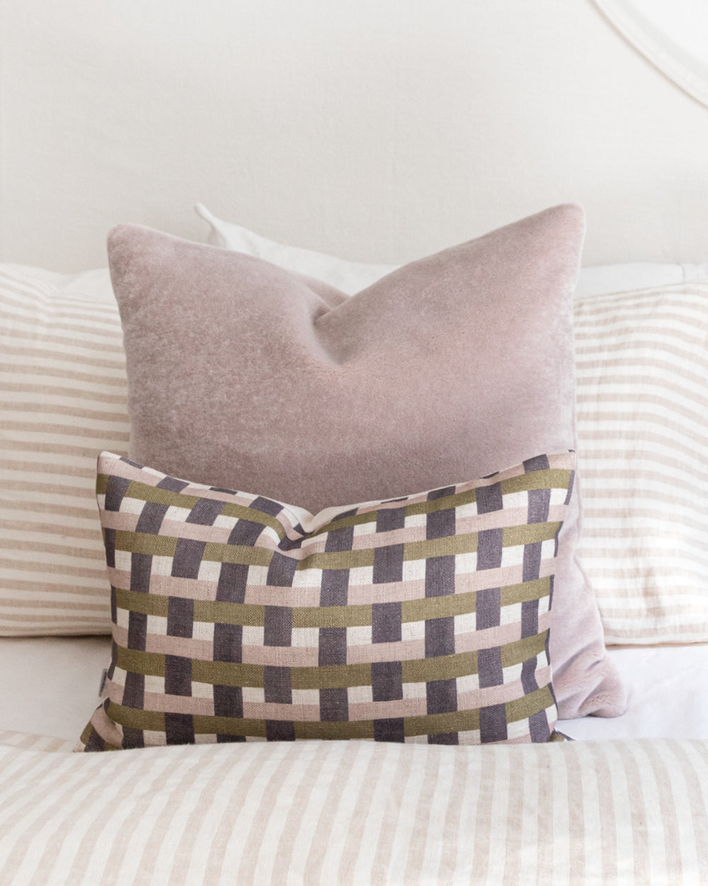 Plum, mauve and olive green check printed pillow sitting on bed with complimentary pink mohair pillow