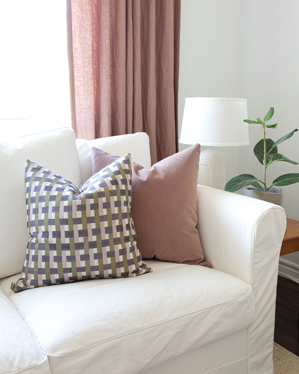 Plum, mauve and olive green check printed pillow sitting on white sofa with pink mohair pillow