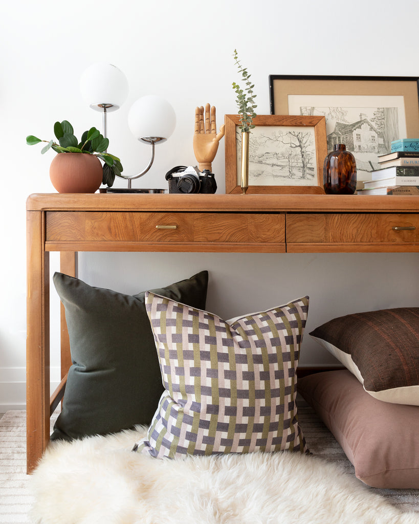 Plum, mauve and olive green check printed pillow sitting under a console table with complimentary green mohair pillow