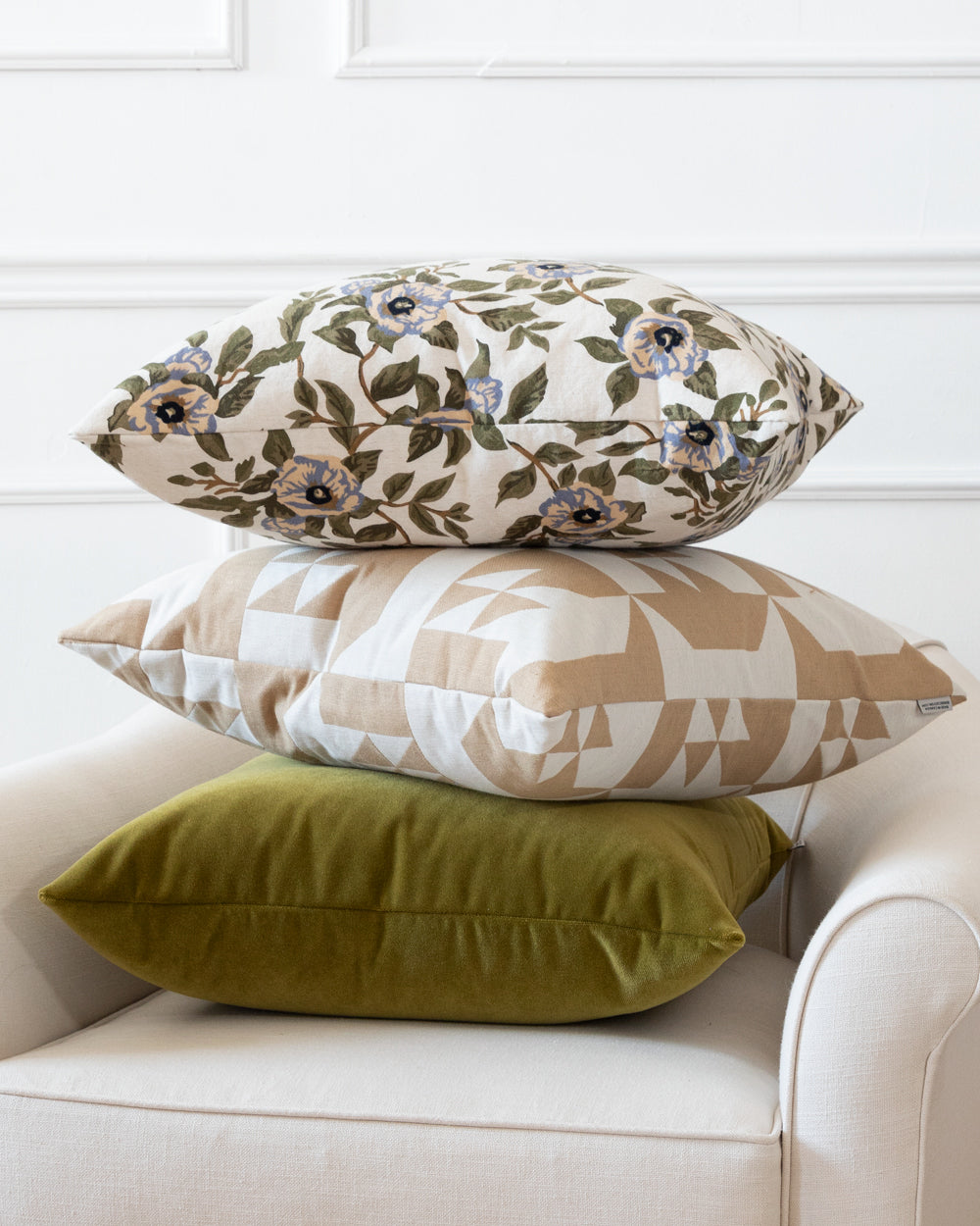 Square cotton floral pillow on top of stack of pillows sitting on a white arm chair