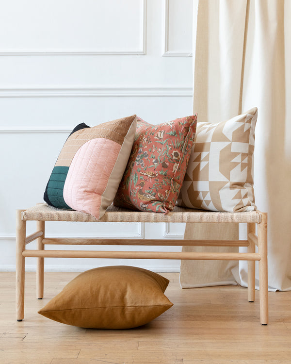 Salmon coloured vintage vintage floral print from the 80s pillow sitting on bench with complimentary quilted pillow and beige geometric pillow