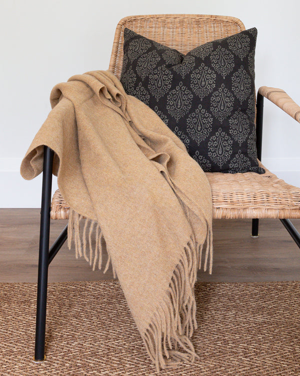 Caramel Alpaca wool throw with tassels on rattan chair with complimentary black Hemme pillow