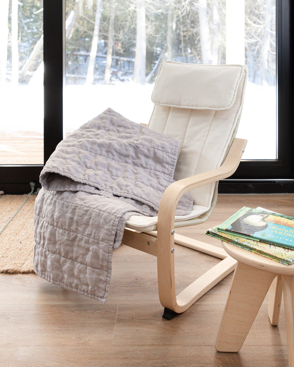 Classic light grey quilt placed on white chair with snowy scene in background