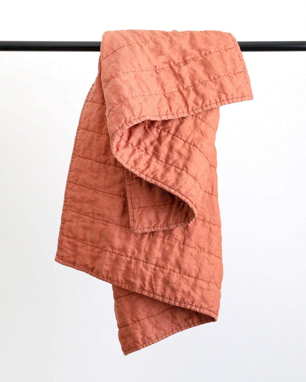 Warm rust colour handmade Linen Quilt folded over black rod