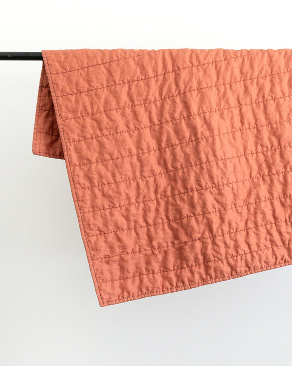 Warm rust colour handmade Linen Quilt folded over black rod