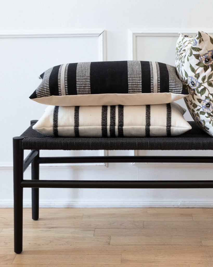 Black and cream striped lumbar pillow sitting on black bench with complimentary pillow