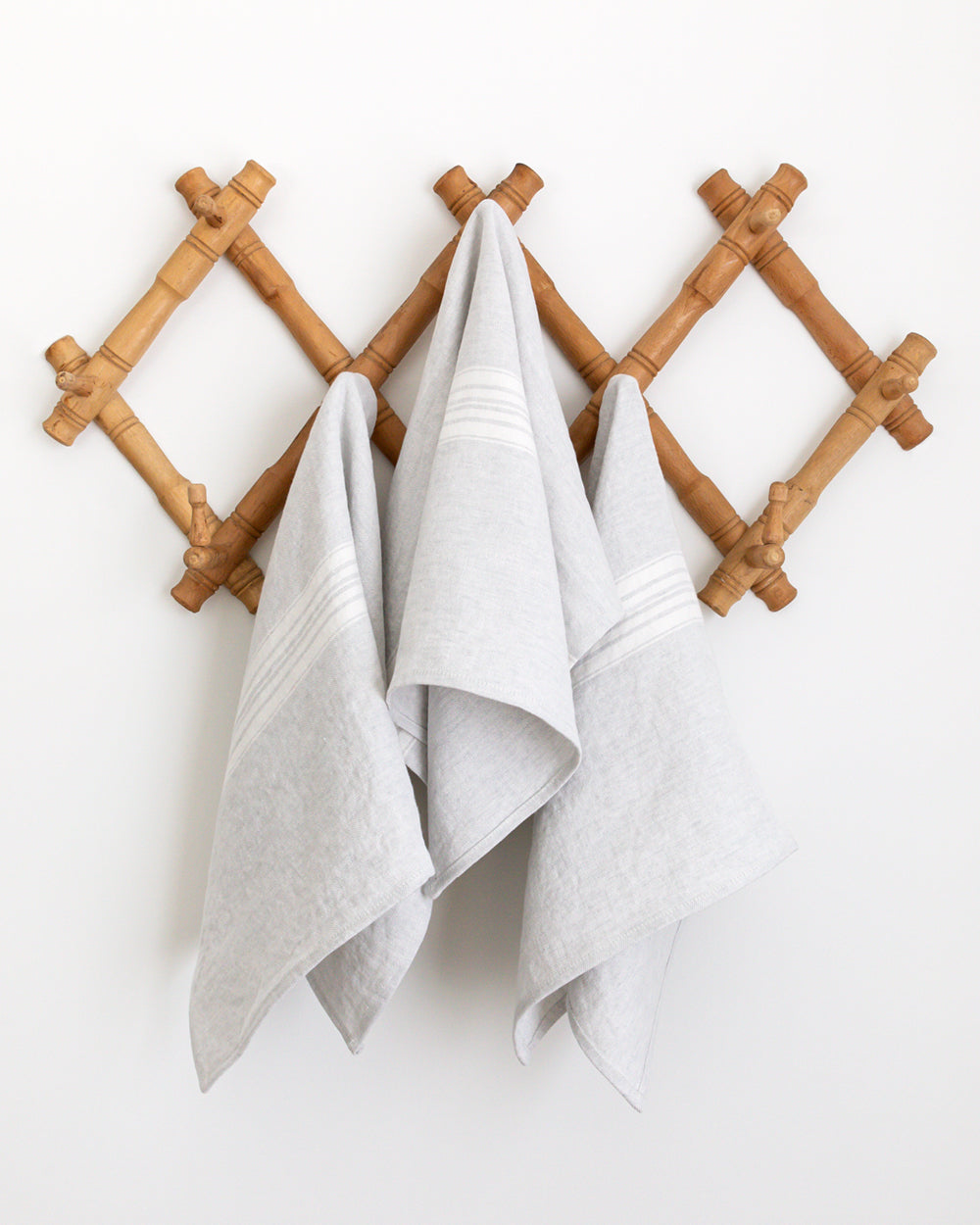 Three stone-washed linen tea towel is a soft, pale grey with a white stripe hanging on wall hooks