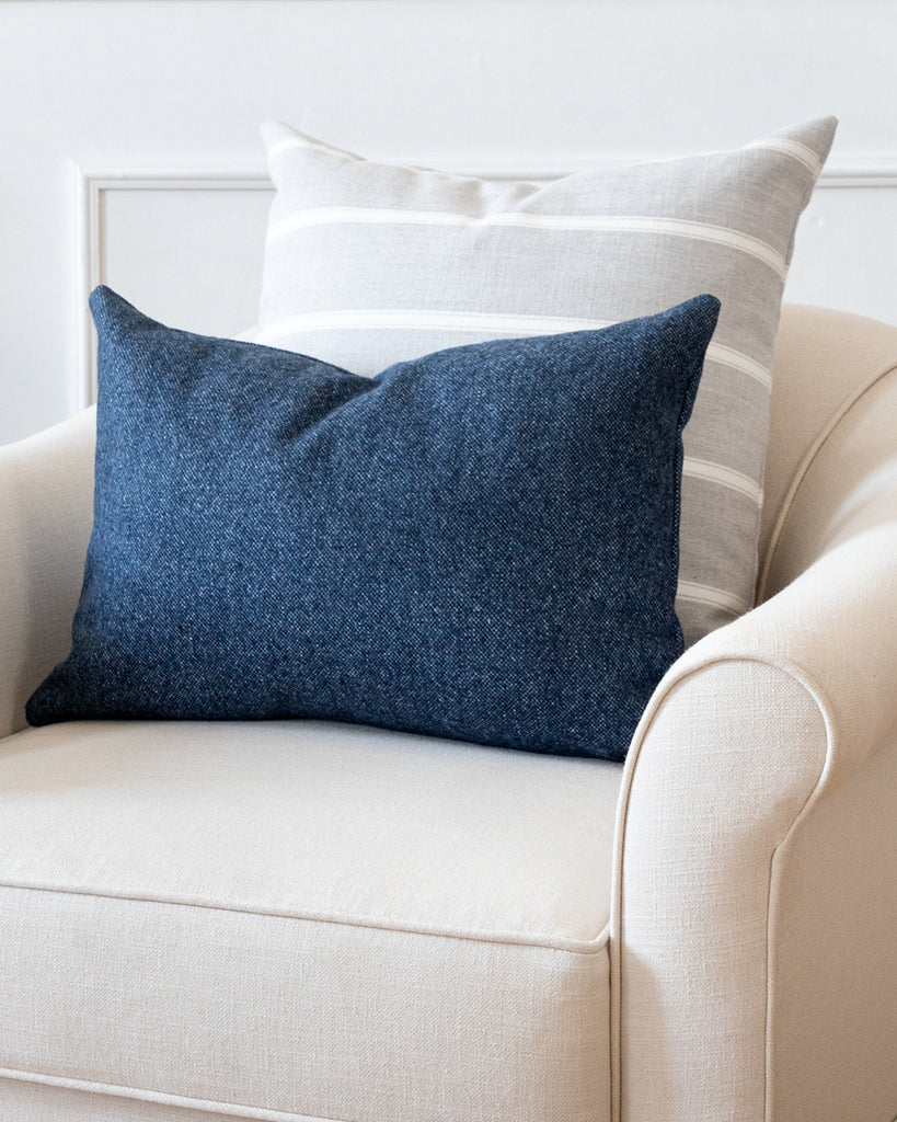 Grey and white striped pillow on white armchair with complimentary Hemme blue pillow