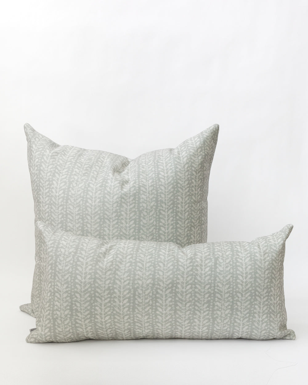 Two pillows with a subtle white floral/vine stripe on a misty grey-blue background