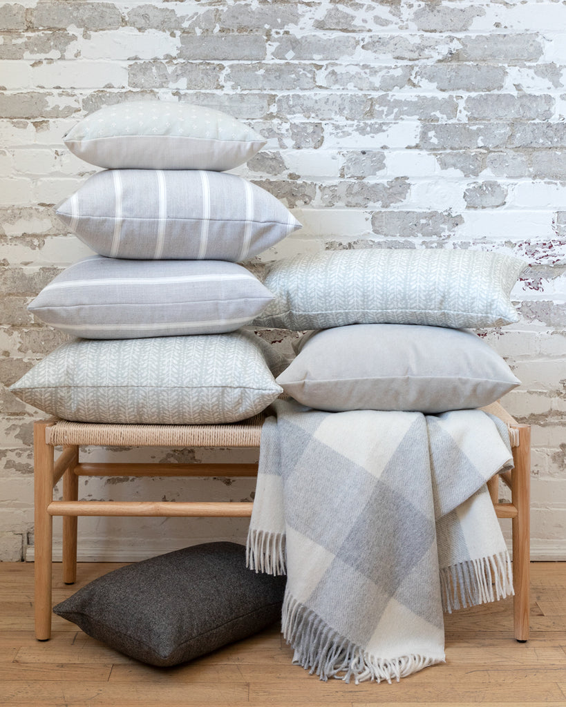 Collection of grey Hemme pillows stacked on bench with grey throw