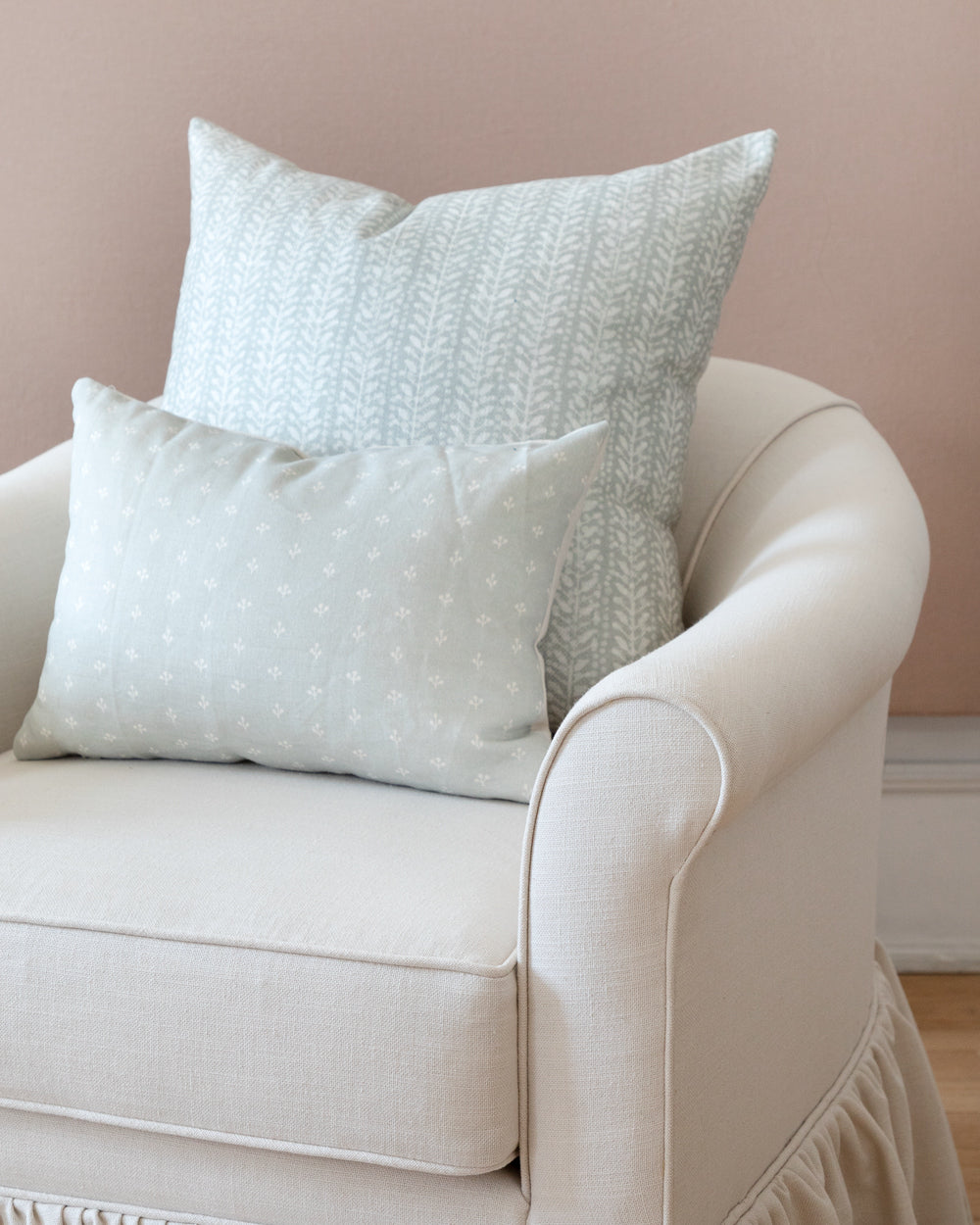 Subtle white floral/vine stripe pillow on a white chair with a complimentary pillow in front
